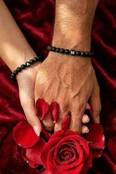 Personalisiertes Partnerarmband Set mit Initialen (A und M) aus matten Onyx-Perlen, gehalten über einer roten Rose als Geschenkidee von Lymaja.