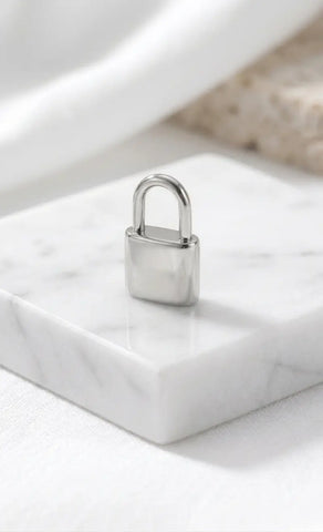 Filigranes, hochglanzpoliertes Liebesschloss-Charm aus silberfarbenem Edelstahl, stehend auf einem eleganten Marmorblock