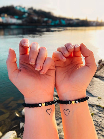 ​Schwarze Partnerarmbänder aus Natursteinperlen mit Initialen-Buchstaben N und S sowie einem goldenem Herz