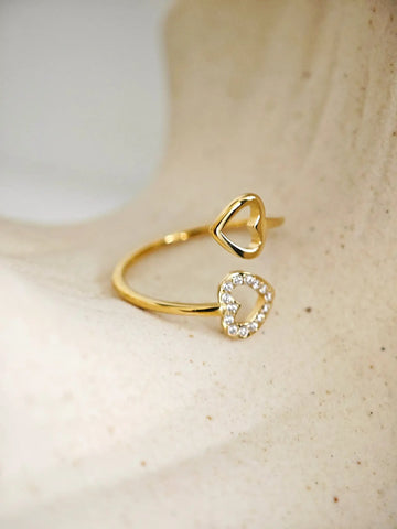 Moderner, offener Wrap-Ring aus goldfarbenem Edelstahl mit zwei Herzen, wovon eines mit funkelnden Zirkona-Steinen besetzt ist.